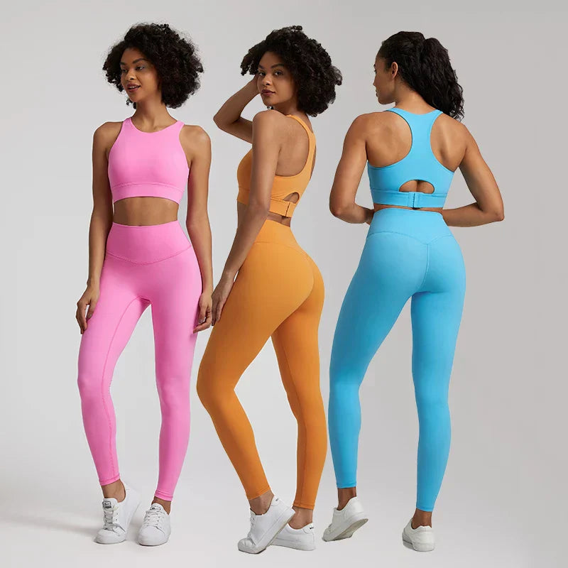 Three women wearing colorful Naked brand seamless leggings and scoop-neck sports bras in pink, orange, and blue, modeled for yoga and workouts